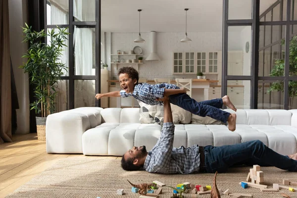 Feliz padre afroamericano levantándose en el aire riendo pequeño hijo. —  Fotos de Stock