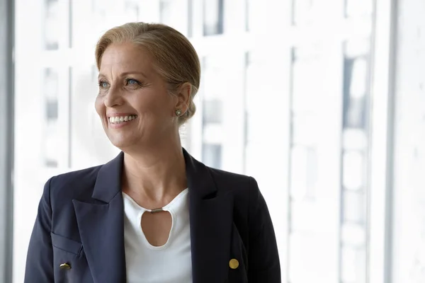 Счастливая женщина-бизнес-лидер позирует у окна офиса, смотрит в сторону — стоковое фото