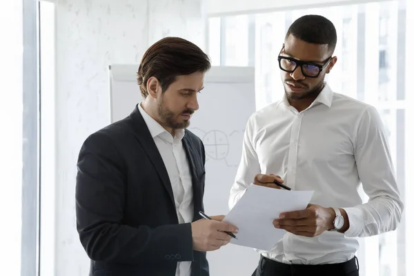 Multiethnic millennial coworkers men reading paper together — Stock Photo, Image