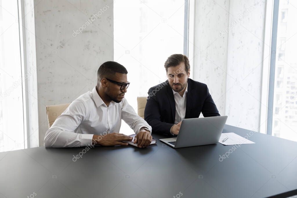 Focused diverse businessmen in formalwear using laptop at office table