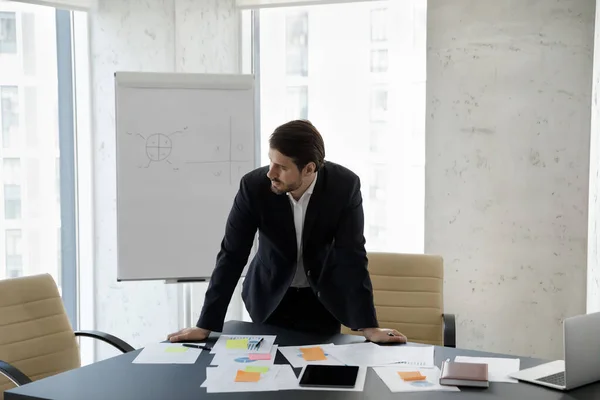 Frustrated concerned business man standing at table with sales reports