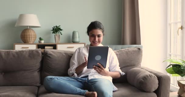Piękna młoda Hinduska kobieta siedzieć na kanapie za pomocą tabletu cyfrowego — Wideo stockowe