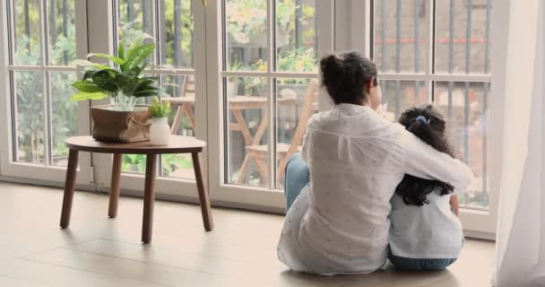 Женщина с заднего вида обнимает дочку, смотрит в окно — стоковое видео