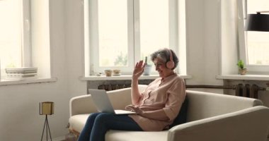Kulaklıklı yaşlı kadın iletişimden zevk alıyor. Laptop ve video çağrısı kullanın.