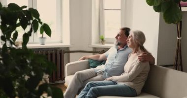 Huzurlu yaşlı çift kanepede oturur ve pencereden dışarı bakarlar.