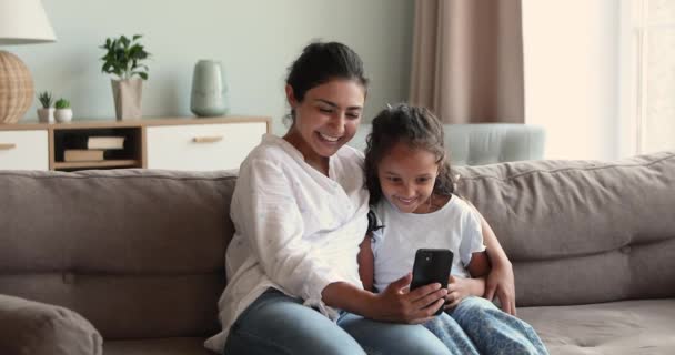 Madre e hija se sientan en el sofá tienen teléfono inteligente de uso divertido — Vídeo de stock