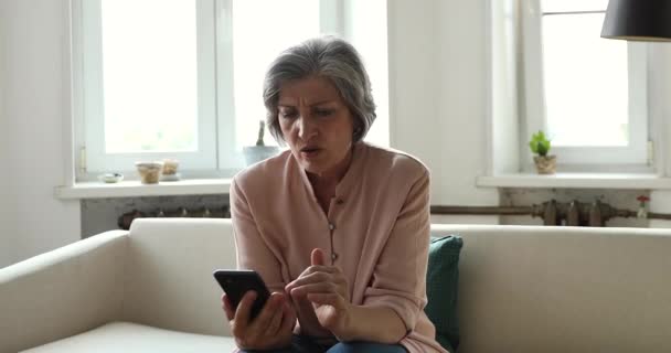 Mujer mayor sosteniendo el teléfono celular leer sms horribles, se ve sorprendido — Vídeos de Stock