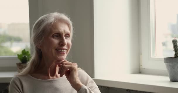 Souriant rêveuse femme âgée coûteuse s'asseoir à l'intérieur regardant dans la distance — Video