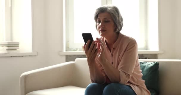 Souriant femme mûre assis sur le canapé en utilisant un téléphone portable — Video