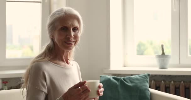 魅力的な年上の女性保持お茶カップ笑顔見ますでカメラ — ストック動画