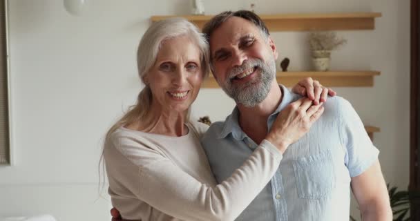 Milující starší pár objímání stojící uvnitř s úsměvem při pohledu do kamery — Stock video