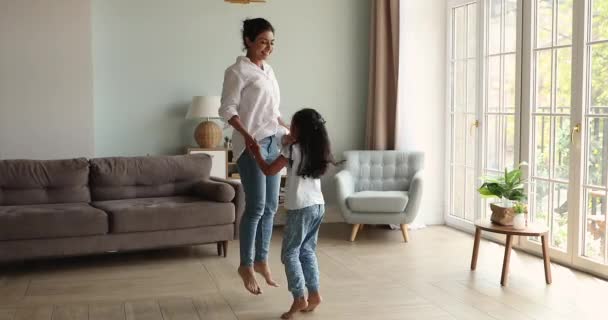 Hintli anne ve küçük kız el ele tutuşup evde zıplıyorlar. — Stok video