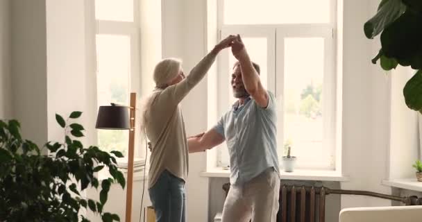 Heureux conjoints actifs plus âgés tenant la main dansant à la maison — Video