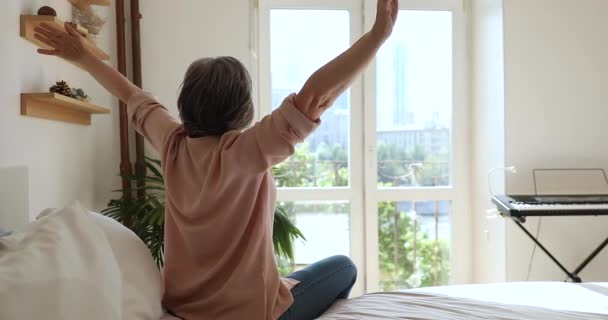 レビュー年上の女性はベッドの上に座る手を上げる幸せな気分 — ストック動画