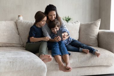 Mutlu anne ve neşeli Z jenerasyonu çocukları dijital cihaz kullanıyor.