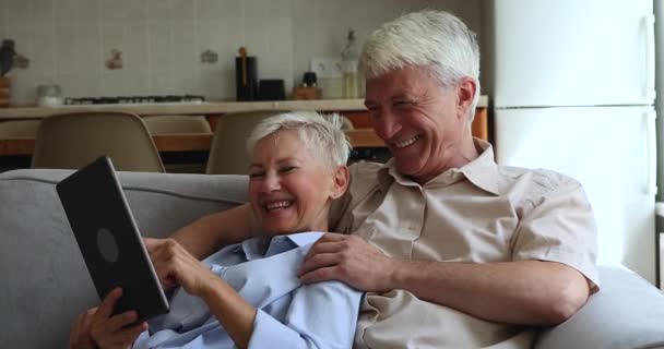 Счастливые пожилые супруги расслабиться на диване весело использовать планшет — стоковое видео