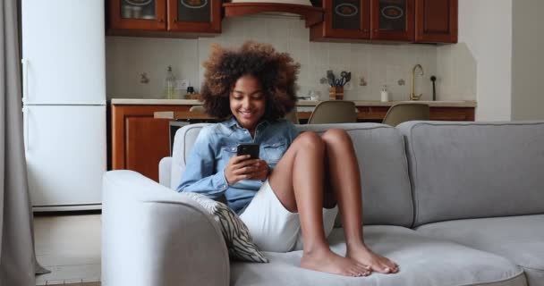 Africano adolescente menina sentar no sofá usar smartphone — Vídeo de Stock