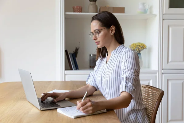 Koncentrerad smart ung kvinna i glasögon studerar på online-kurser. — Stockfoto