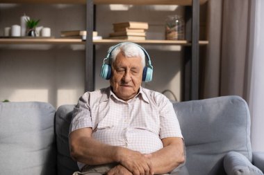 Yorgun yaşlı adam büyük kablosuz kulaklıklardan müzik dinliyor.