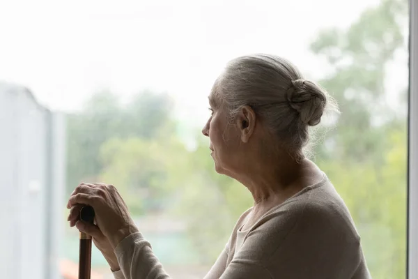 Hüsrana uğramış üzgün, yalnız, yaşlı kadın cam kenarında oturuyor. — Stok fotoğraf
