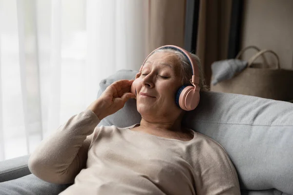 Huzurlu yaşlı hayran kadın son moda kulaklıklardan müzik dinliyor. — Stok fotoğraf