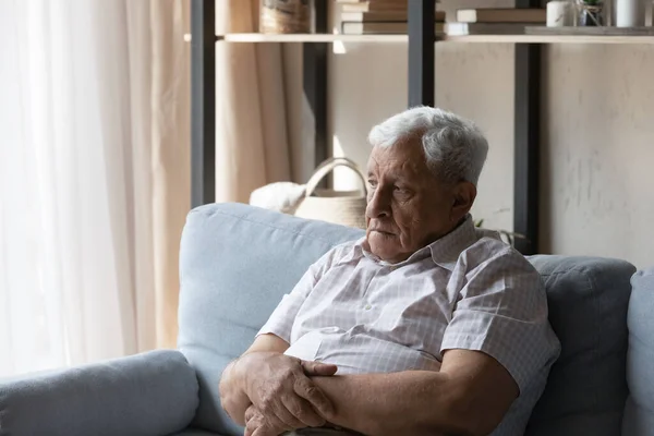 Sfrustrowany starszy 80-letni mężczyzna siedzi na kanapie w domu — Zdjęcie stockowe