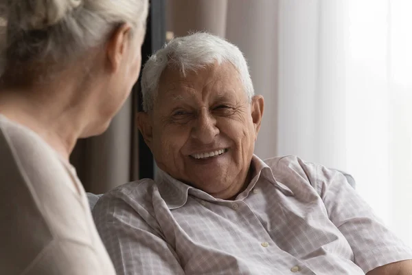 Homem idoso feliz conversando com a esposa, cuidador feminino em casa — Fotografia de Stock