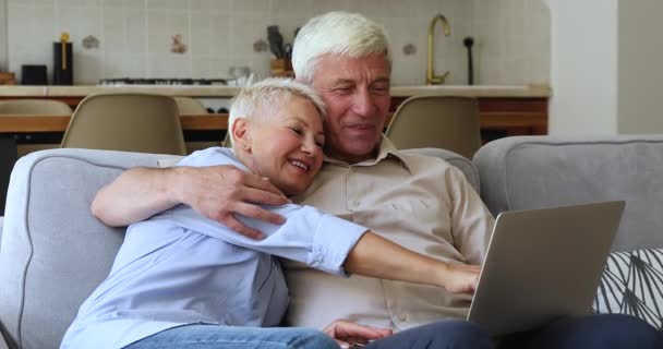 Счастливая пожилая пара расслабиться на диване купить товары с помощью ноутбука — стоковое видео