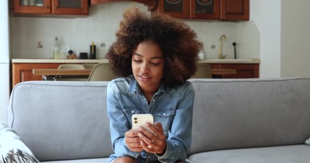 Africana adolescente sentarse en sofá mensajes de texto SMS utilizar el teléfono celular — Vídeo de stock