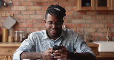 Gülümseyen Afrikalı Amerikalı erkek hipster mutfakta telefon uygulaması kullanıyor.