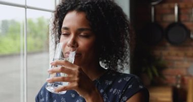 Sağlıklı genç Afrikalı kadın mutfakta camdan su içiyor.