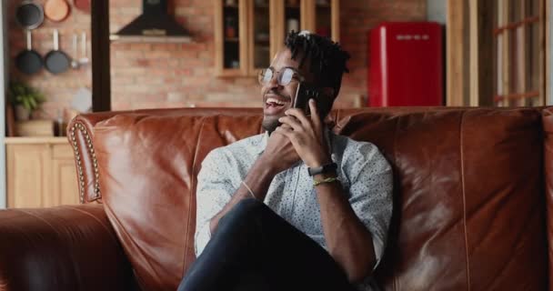 Millennial Afro American guy sit on sofa chat on phone — Stock video