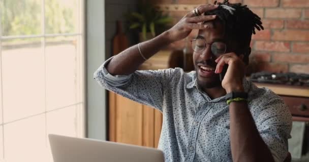 Genç siyahi erkek serbest çalışan dizüstü bilgisayarın önünde telefon görüşmesi yapıyor. — Stok video