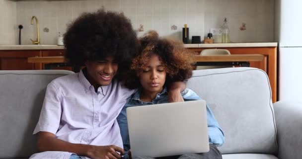 Подростковая африканская пара сидит на диване и разговаривает с помощью ноутбука — стоковое видео