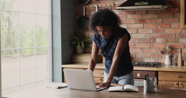 Pensive afro amerikanska kvinnliga stå vid köksbordet använda laptop — Stockvideo