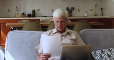 Ciddi yaşlı adam banka evraklarını kontrol ediyor, kamu hizmetlerini inceliyor, endişeli görünüyor.