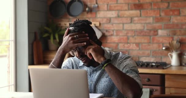 Jovem Africano positivo bate-papo no telefone distraído do laptop — Vídeo de Stock