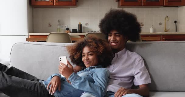 Bella coppia di adolescenti africani rilassarsi sul divano con gadget — Video Stock
