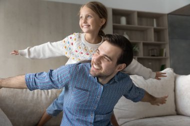 Neşeli baba ve mutlu kız çocuk kanepede uçak oyunu oynuyorlar.