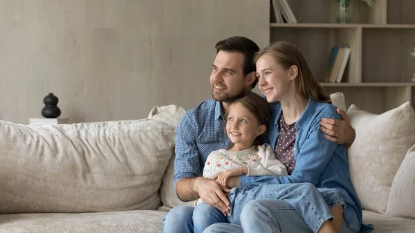 Dromerige ouders en lieve dochter meisje zitten op de bank — Stockfoto