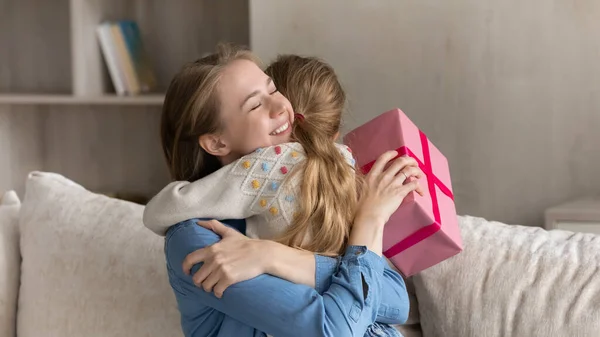 Glückliche überglückliche Mutter hält rosa Geschenkkarton in der Hand, umarmt kleine Tochter — Stockfoto