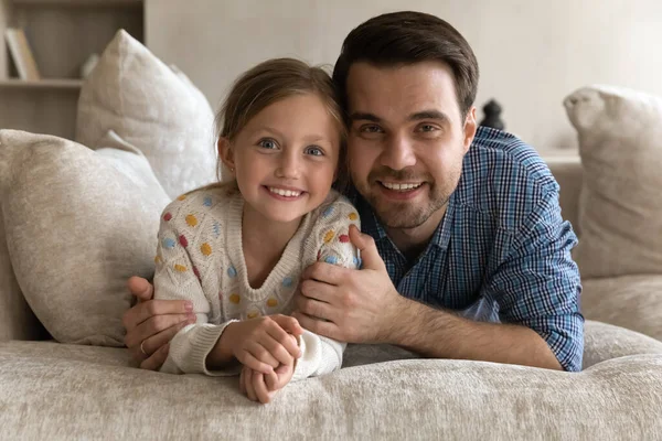 Radosny tata obejmujący szczęśliwą córeczkę, leżącą na wygodnej kanapie — Zdjęcie stockowe