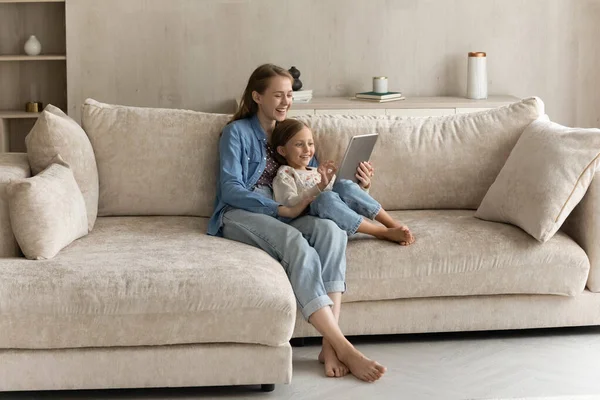 Glückliche junge Mutter umarmt süßes Töchterchen auf bequemer Couch — Stockfoto