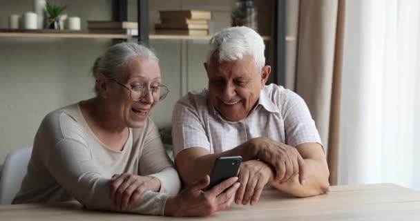 Улыбающаяся пара смотрит на экран мобильного телефона смотреть смешные видео в Интернете — стоковое видео