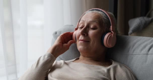 Yaşlı kadın kaliteli sesten hoşlanıyor, kulaklıkla en sevdiği müziği dinliyor. — Stok video