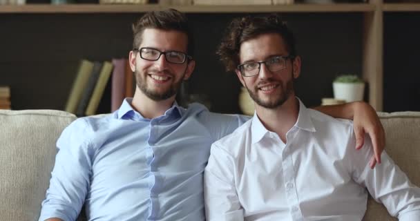 İki mutlu genç adam, dost canlısı ikiz kardeşler kanepede kucaklaşır. — Stok video