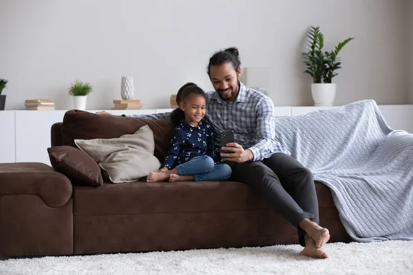 Heureux jeune homme afro-américain utilisant un téléphone portable avec sa fille. — Photo