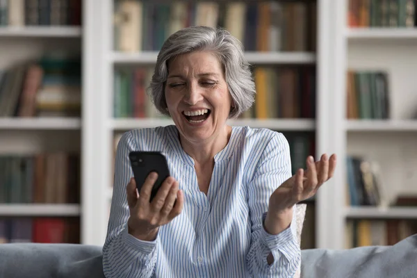 Překvapený šťastný zralý žena smích pomocí mobilu doma. — Stock fotografie