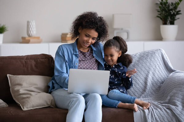 Smiling affectionate young African American mother using computer with little daughter.