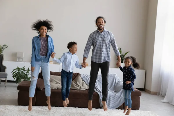 Feliz activa familia afroamericana saltando en la sala de estar moderna. — Foto de Stock